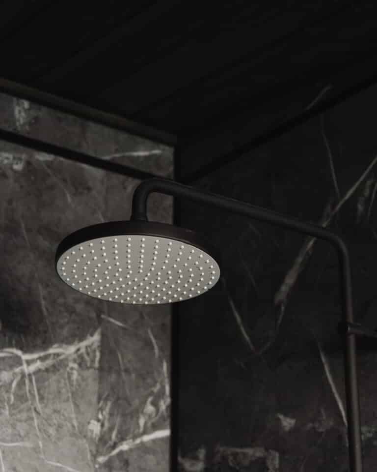 Pyöreä, musta sadesuihkupää on asennettu tummaa marmorilaattaseinää vasten modernissa saunamökin kylpyhuoneessa, jossa tyyli ja mukavuus yhdistyvät.