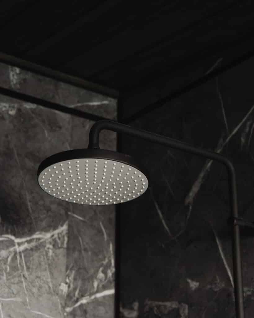 Pyöreä, musta sadesuihkupää on asennettu tummaa marmorilaattaseinää vasten modernissa saunamökin kylpyhuoneessa, jossa tyyli ja mukavuus yhdistyvät.