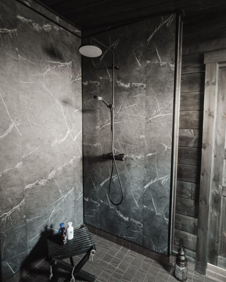 Moderni suihku, jossa on harmaat marmoriseinät, sadesuihkupää ja käsisuihku. Pieni pöytä, jossa on kylpytuotteita, on lähellä, ja lattia on kaakeloitu.