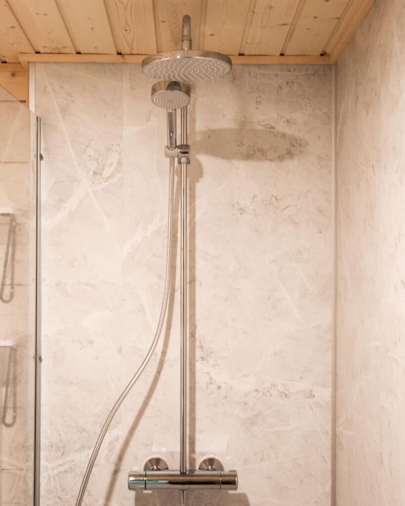 Moderni suihkulaite, jossa on suuri sadesuihkupää ja käsisuihku, joka täydentää täydellisesti valmis kylpyhuoneen muotoilua laatoitetulla kylpyhuoneen seinällä.
