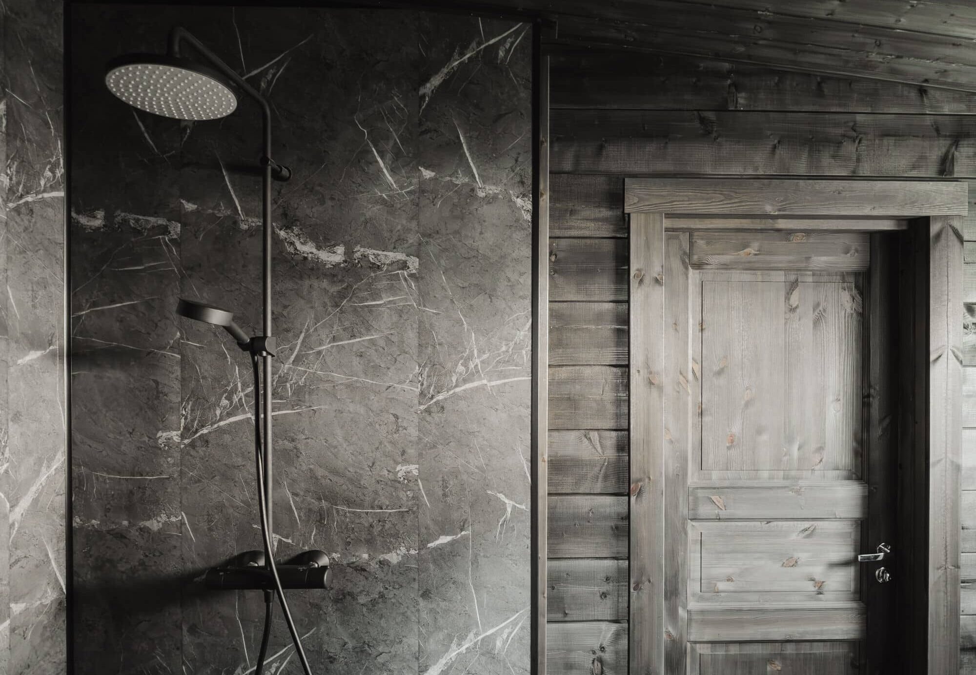 Ehta hirsisaunan valmiskylpyhuone. Tummat marmoria mukailevat seinälaatat ja Oraksen mattamusta sadesuihku luovat hienostuneen tunnelman tumman hirsisaunan yhteyteen.