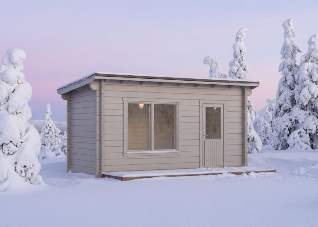 Pieni, vaalea puinen mökki, jossa on suuret ikkunat, sijaitsee lumisessa maisemassa lumisten puiden ympäröimänä pastellivärisen taivaan alla - viehättävä pihasauna, joka sopii täydellisesti rentoutumiseen talvipäivän jälkeen.