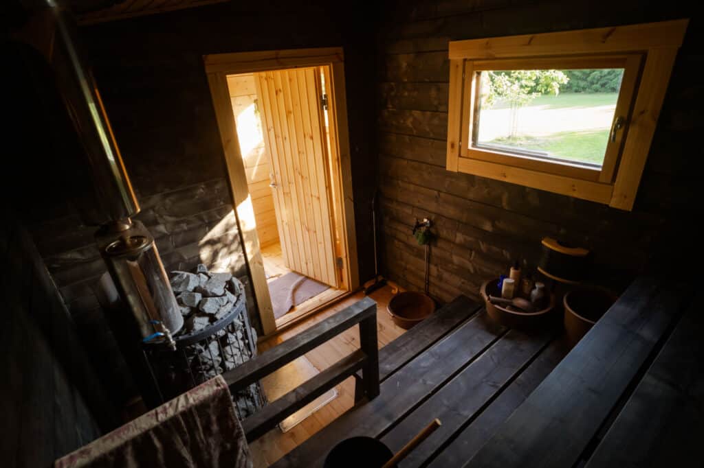 Pihasauna 10:n tummasävyinen löylyhuone, jossa kiuas ja ikkuna