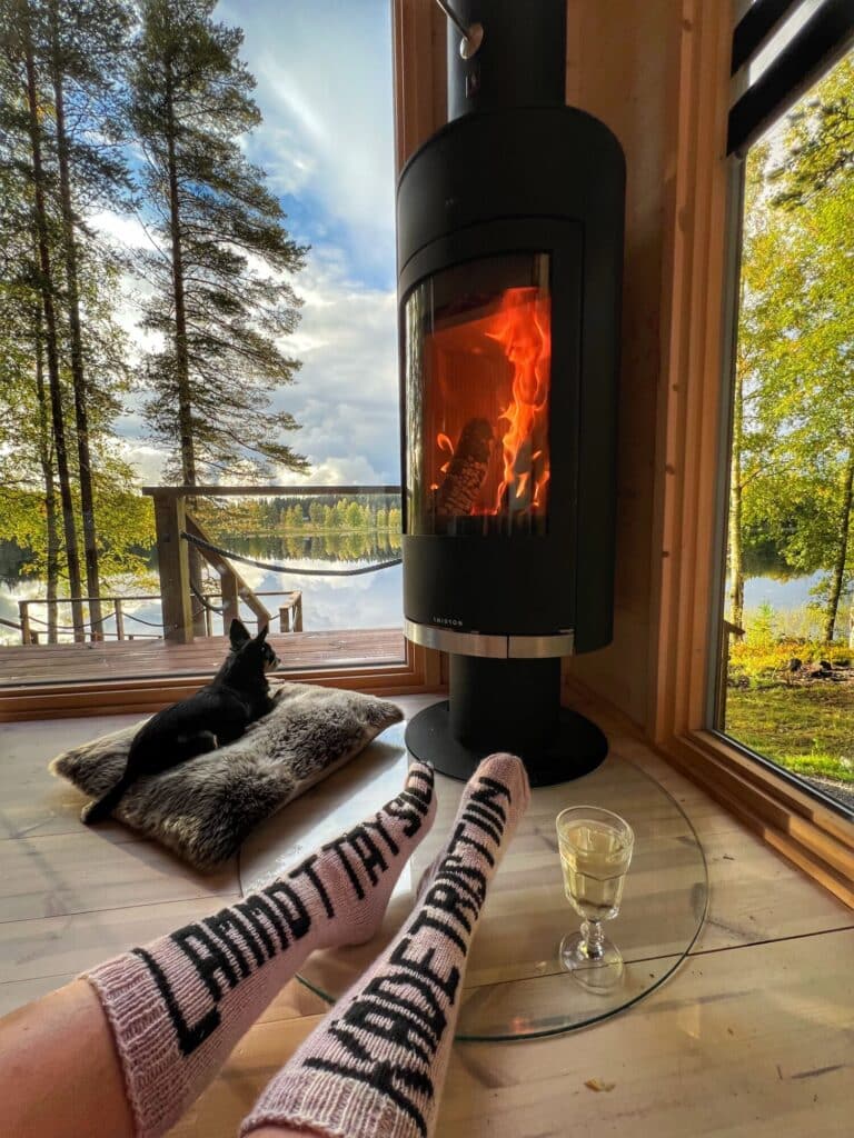 Takka loimuaa Ehta-aitan lasiseinän vieressä, ikkunasta järvi- ja metsämaisema