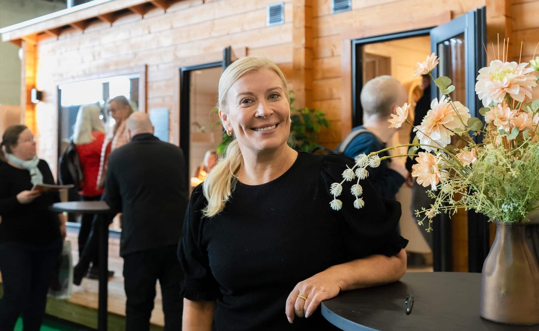 Kirsi Alm-Siira hymyilee tyylikkäässä, tummassa asussa Ehta -messumökin edustalla. Kirsi antoi vinkkejä saunamökin suunnitteluun ja hankintaan Kevätmessuilla 2025