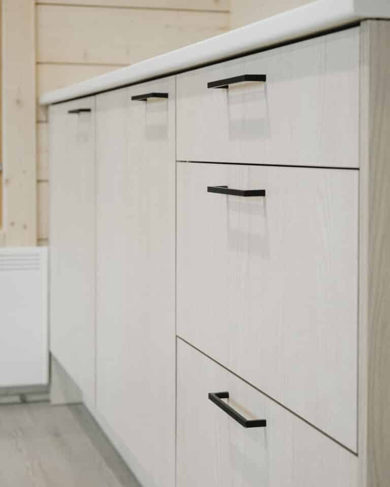 Vaaleat puiset keittiökaapit, mustat kahvat ja valkoinen työtaso modernissa, minimalistisessa sisustuksessa.