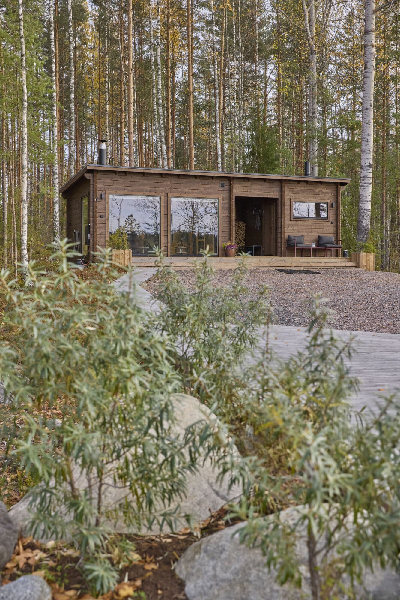 Rantasauna ilman rakennuslupaa voi olla maailman helpoin projekti kun rakennus tilataan vielä valmistoimituksena. Jämsästen hankkima moderni Ehta-saunamökki isoilla maisemaikkunoilla kohoaa ylväänä Heinolan Vasikkasaaren rannassa, perinteinen sekametsä häämöttää taustalla. Ruskeaksi kuultomaalattu hirsipinta sulautuu mäntymaisemaan. Rannasta kulkee polku mökin koko edustan mittaiselle terassille.