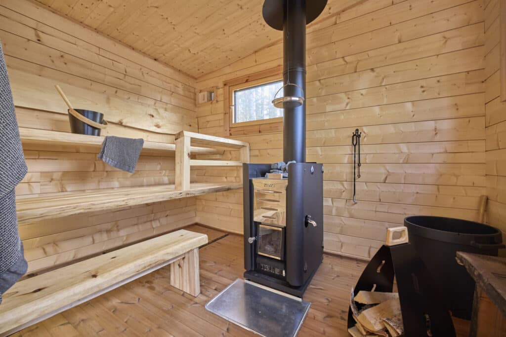 Puupaneloitu saunatupa, jossa on puukiuas, penkki, kauha ja kauha, polttopuuvarasto ja pieni ikkuna.