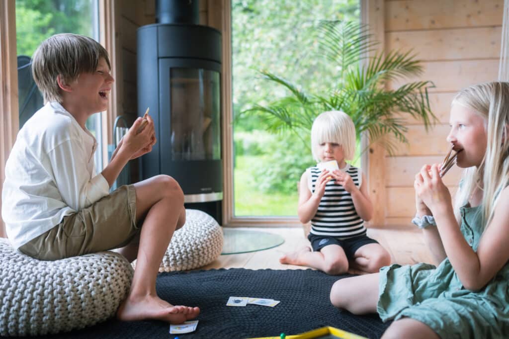 Kolme lasta istuu lattialla viihtyisässä huoneessa hymyillen ja syöden välipaloja, ja heidän eteensä on ripoteltu pelikortteja, jotka tuovat mieleen huolettomia päiviä, joita vietettiin villatissa tai aitatissa perheen lomamatkoilla.